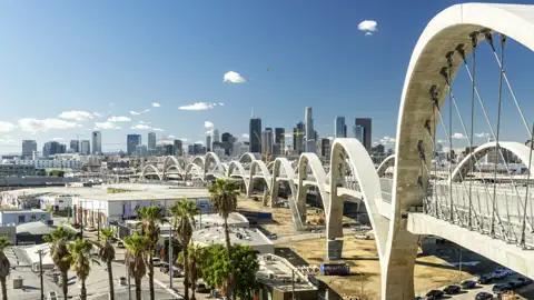 Die markante Bogenarchitektur der Sixth Street Viaduct vor der sonnigen Skyline von Downtown Los Angeles mit Palmen, ein toller Anblick auf unserer Rundreise mit Studiosus.