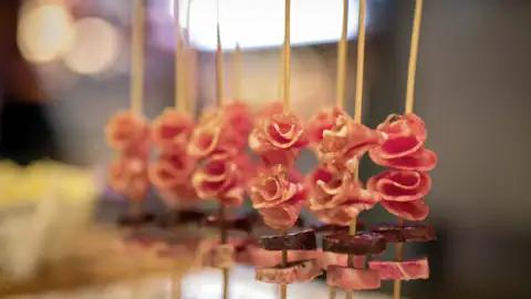 Nahaufnahme von kunstvoll zubereiteten Pintxos im Baskenland: Holzspieße mit Rosen aus Schinken und Wurststückchen, ein kulinarische Highlight auf unserer Kulturreise mit Studiosus nach Barcelona.