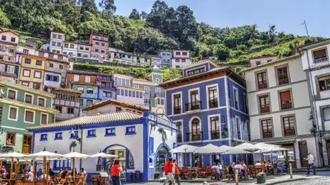 Sonnige Plaza im Fischerdorf Cudillero in Asturien mit bunten Häusern am Hang und belebten Terrassen von Cafés, ein Hingucker auf unserer Kulturreise mit Studiosus.