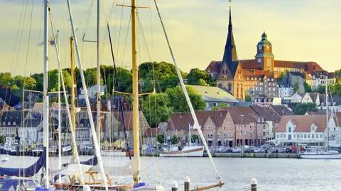 Segelboote im Flensburger Hafen vor den Giebelhäusern der Altstadt, über die der Turm der Marienkirche ragt, ein Highlight unserer Gruppenreise nach Norddeutschland.