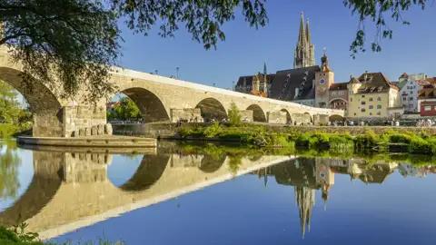 Die Steinerne Brücke in Regensburg mit dem Dom St. Peter im Hintergrund, gespiegelt im ruhigen Wasser der Donau, ein Highlight unserer Studiosus Rundreise.