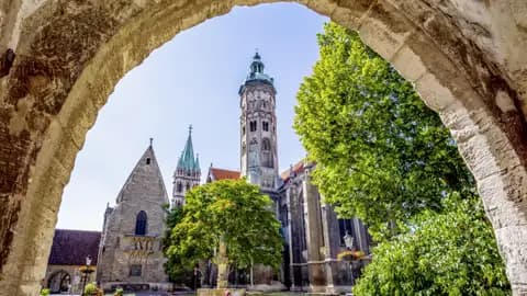 Studienreise nach Sachsen-Anhalt: Blick durch einen alten Torbogen auf den berühmten Naumburger Dom bei blauem Himmel.
