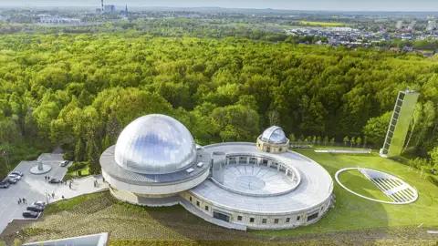 Vogelperspektive auf das Schlesische Planetarium bei Kattowitz mit seiner silbernen Kuppel inmitten einer dichten Waldlandschaft, ein Highlight unserer Rundreise mit Studiosus nach Polen.