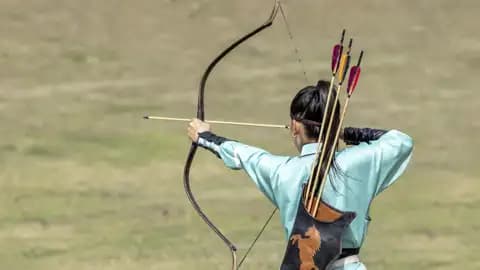 Rückansicht einer Bogenschützin in hellblauer Tracht, die bei den World Nomad Games in Kirgisistan einen Pfeil anlegt, ein Highlight unserer Gruppenreise mit Studiosus.