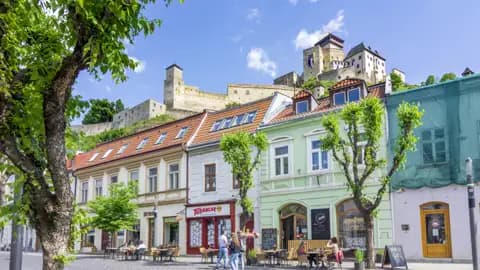 Häuserzeile mit bunten Fassaden und Cafés in der Altstadt von Trencin, darüber thront die mächtige Burg Trencin, ein Highlight unserer Gruppenreise mit Studiosus.