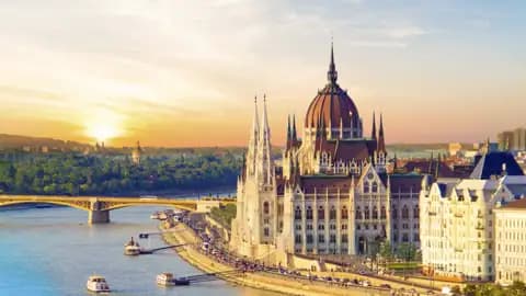 Das ungarische Parlamentsgebäude in Budapest am Donauufer im goldenen Licht des Sonnenuntergangs, Ausflugsboote auf dem Fluss, ein Ausblick, den wir auf einer Studiosus Rundreise genießen.