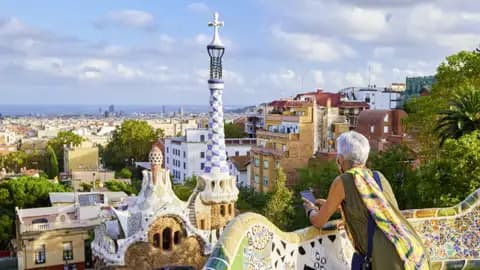 Auf unserer Gruppenreise mit Studiosus genießt eine Reisende auf der berühmten Mosaikbank im Parc Güell den weiten Blick über die Dächer von Barcelona.