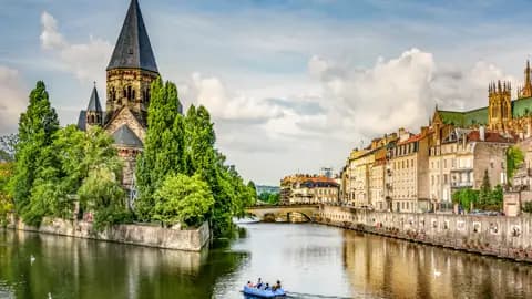 Der historische Temple Neuf in Metz auf einer kleinen Insel der Mosel, davor ein Ausflugsboot und die Altstadtfassaden, ein Highlight auf unserer Gruppeneise mit Studiosus.