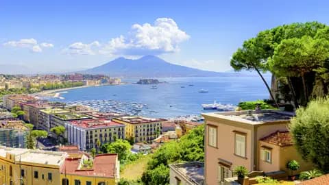 Sonnige Aussicht über den Golf von Neapel mit Jachthafen, bunten Häusern und dem majestätischen Vulkan Vesuv am Horizont, ein Highlight unserer Gruppenreise mit Studiosus.