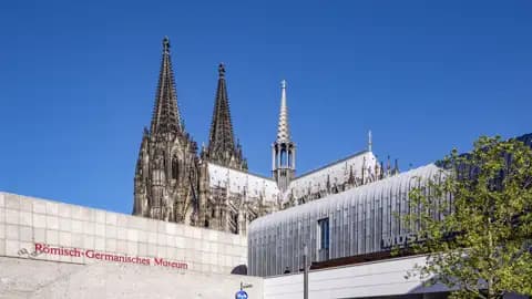 Entdecken Sie den Architektonischer Kontrast auf Ihrer Studienreise in Köln: Die gotischen Spitzen des Doms ragen hinter dem Museum Ludwig und dem Römisch-Germanischen Museum auf.