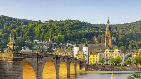 Auf unserer Gruppenreise mit Studiosus bewundern wir die Alte Brücke über den Neckar in Heidelberg, von der Morgensonne beleuchtet, mit der Heiliggeistkirche und der Altstadt.