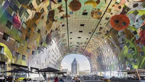 Besucher einer Studienreise unter der riesigen, gewölbten Decke der Markthalle in Rotterdam mit ihrem bunten Kunstwerk.