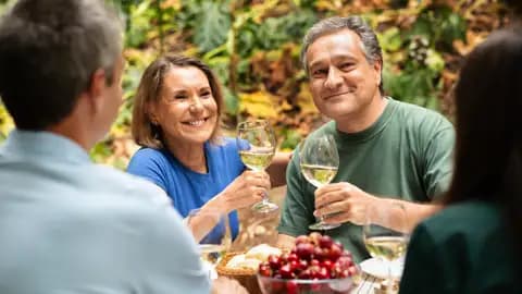 Ein lächelndes Paar bei einer Weinverkostung auf einer Studienreise im Elsass, mit Weißweingläsern am Tisch im Freien.