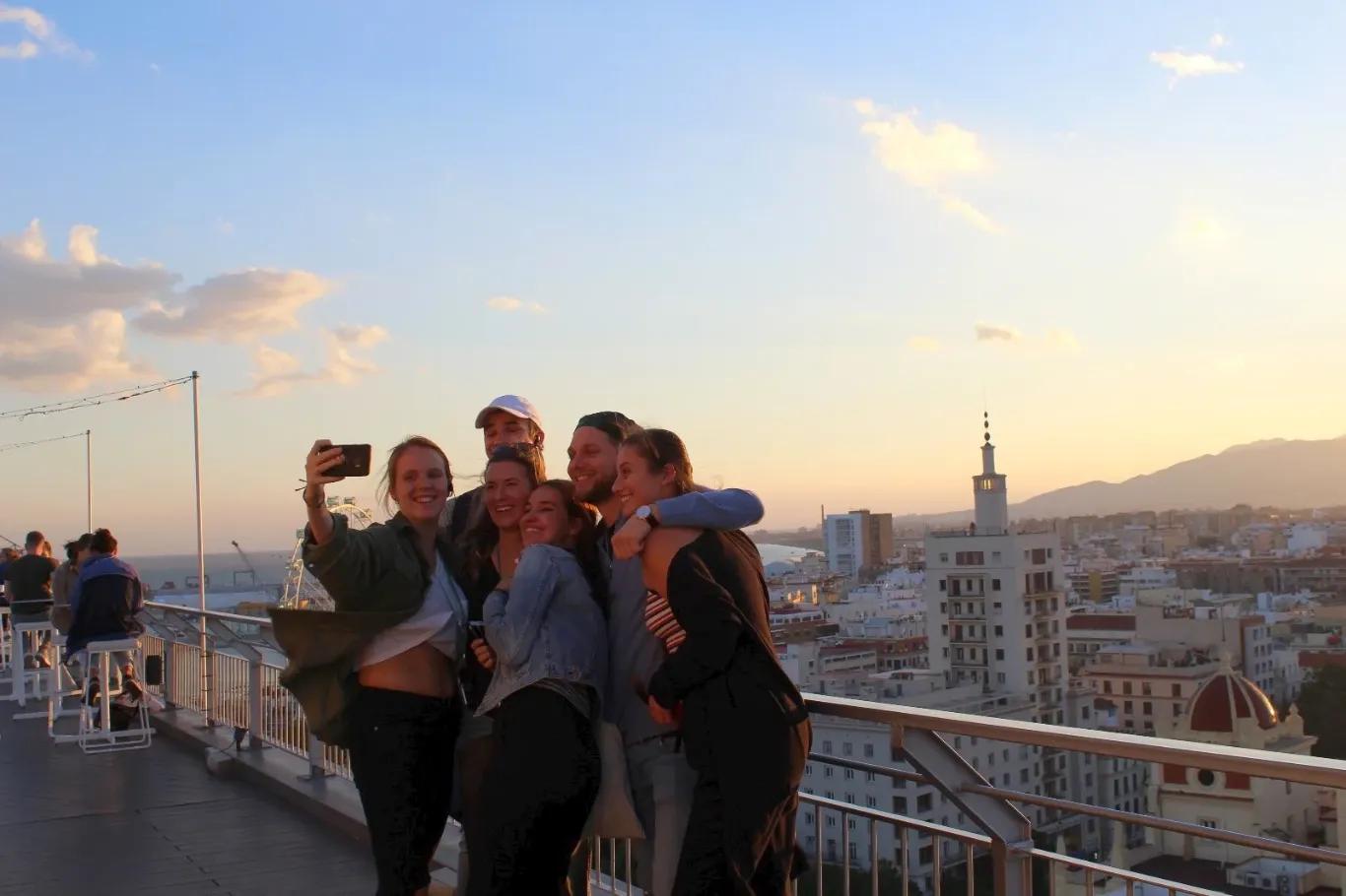 Gruppe von Auszubildenden posiert für ein Selbstporträt vor einer Stadtlandschaft bei Sonnenuntergang.