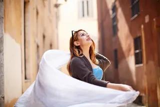 Eine Frau, die in der Sonne steht und einen weißen Schal umherwirbelt.