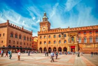 Blick auf die belebte Piazza Maggiore in Bologna mit historischem Rathaus mit Glockenturm.