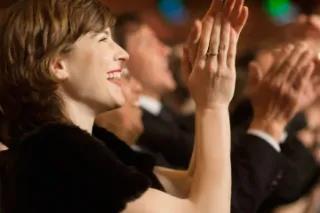 Eine Frau mit fröhlichem Gesichtsausdruck applaudiert begeistert.