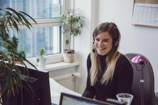 Frau mit Headset lächelt an ihrem Arbeitsplatz