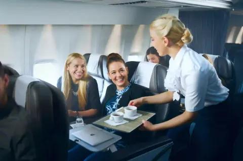 Eine Stewardess serviert Kaffee an Passagiere in einem Flugzeug.