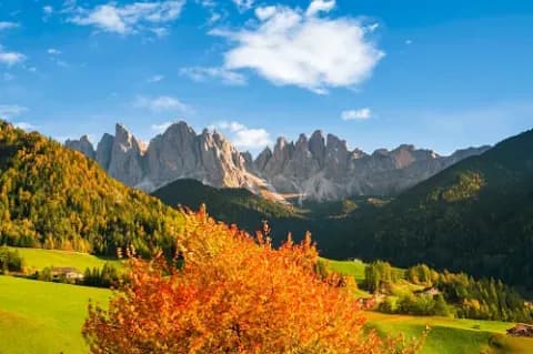Eine herbstliche Landschaft in Südtirol mit Bergen und einigen wenigen Häusern ist zu sehen.