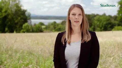 Eine Frau steht in einem Feld mit Bäumen im Hintergrund.