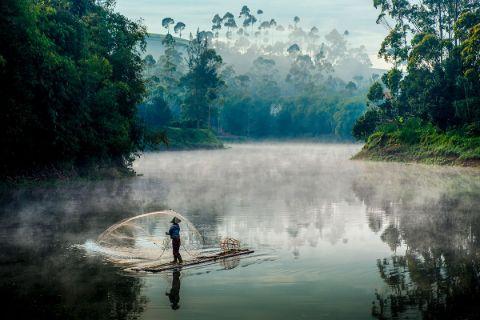 Ein Fischer, der im Nebel auf einem ruhigen Fluss fängt.