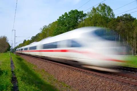 Ein Moderner ICE Zug fährt schnell durch die Landschaft und hinterlässt eine verschwommene Bewegung.