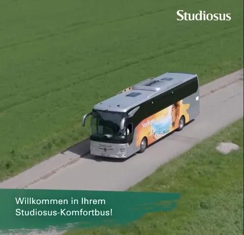 Der Komfortbus von Studiosus fährt auf einer Landstraße durch ein grünes Feld.