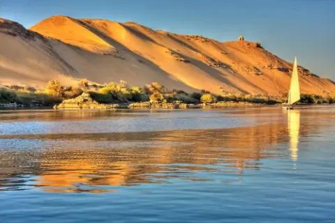 Sonnenuntergang über dem Nil mit einem Segelboot und Sanddünen.