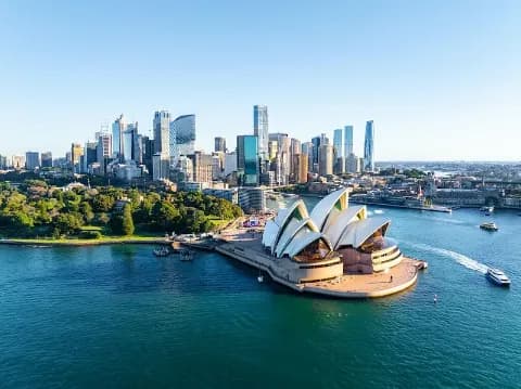 Ein Panoramablick auf der Skyline von Sydney mit dem berühmten Sydney Opera House am Wasser im Vordergrund.