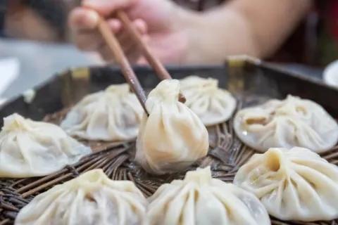 Nahaufnahme von Dumplings, die mit Essstäbchen aufgenommen werden.