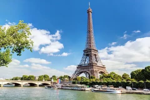 Der Eiffelturm in Paris am Ufer der Seine mit Rundfahrtbooten im Vordergrund.
