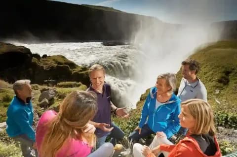 Eine Gruppe von Menschen, die bei sonnigem Wetter an einem Wasserfall stehen und sich unterhalten.