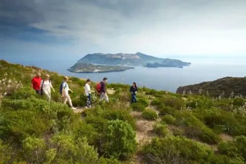 Sechs Personen wandern durch eine hügelige Landschaft mit Meerblick.
