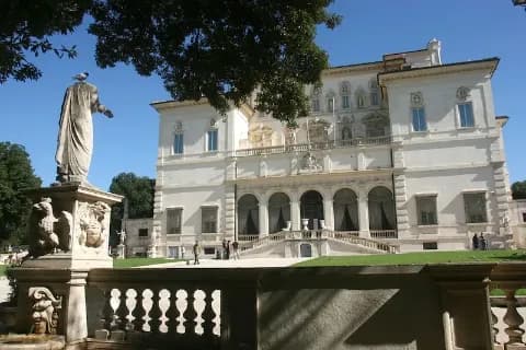 Ansicht der Villa Borghese in Rom mit einer Statue und Garten im Vordergrund.