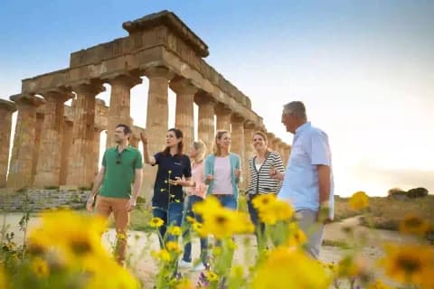 Eine Reisegruppe mit Reiseleiterin steht vor antiken Säulen beim Sonnenuntergang.