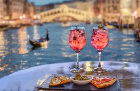 Erfrischende Cocktails, Pizza und Oliven auf einem Tisch mit Blick auf den Grand Canal in Venedig am Abend.