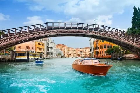 Ein Holzboot fährt unter einer Brücke durch einen Kanal in Venedig.
