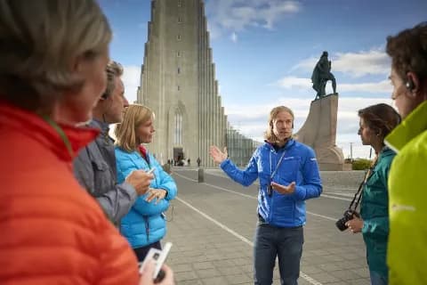 Studiosus Reisegruppe steht im Halbkreis um ihren Reiseleiter und hört spannende Fakten über die Hallgrimskirche.