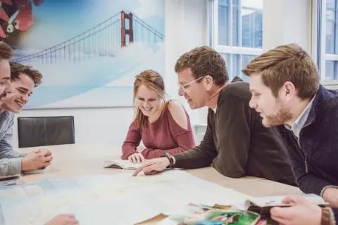 Gruppe von Menschen brainstormen kreative Reiseideen anhand einer Karte.