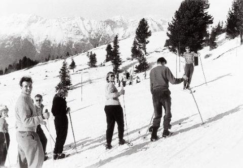 Skifahrer auf einer alpinen Piste, umgeben von schneebedeckten Bäumen und Bergen.