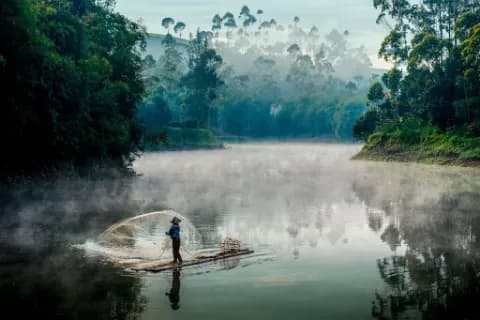 Ein Fischer, der im Nebel auf einem ruhigen Fluss fängt.