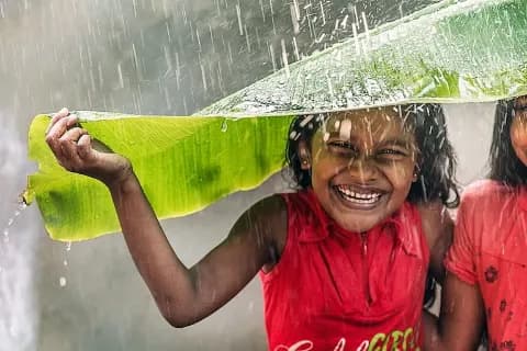 Portrait eines lachenden Kindes, das sich mit einem Bananenblatt vor dem Regen schützt.