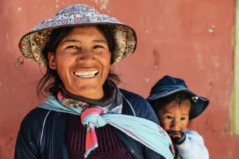 Portrait einer lachenden peruanischen Frau mit Kleinkind auf dem Rücken.