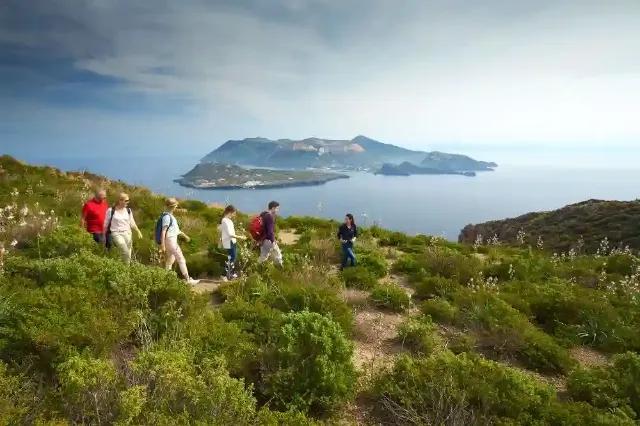 Sechs Personen wandern durch eine hügelige Landschaft mit Meerblick.