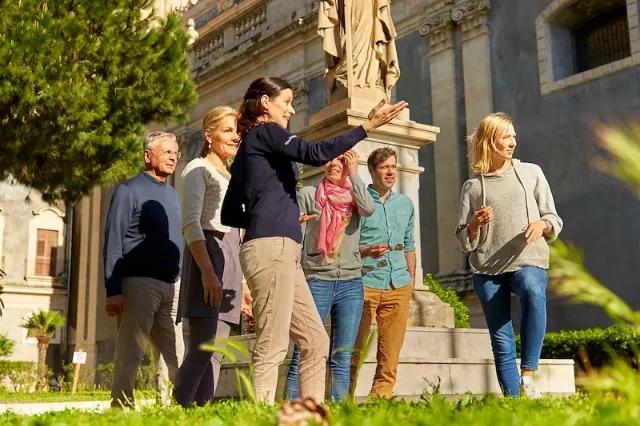 Eine Reisegruppe ist mit einer Reiseleiterin bei sonnigem Wetter unterwegs.