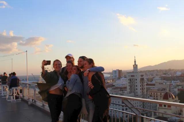 Gruppe von Auszubildenden posiert für ein Selbstporträt vor einer Stadtlandschaft bei Sonnenuntergang.