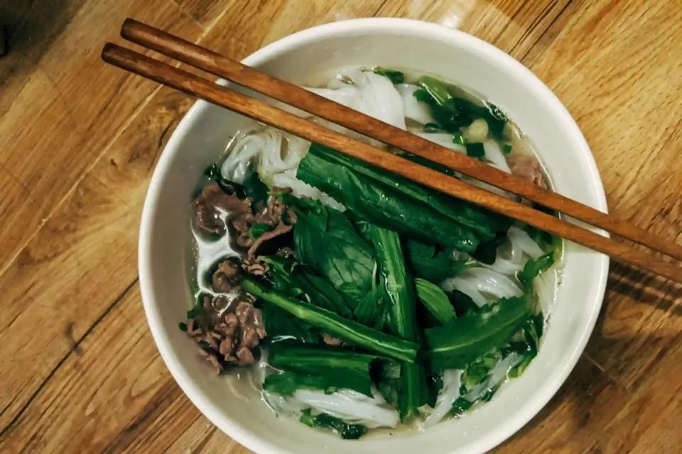 Schüssel mit vietnamesischer Nudelsuppe, frischen Kräutern und Rindfleisch.