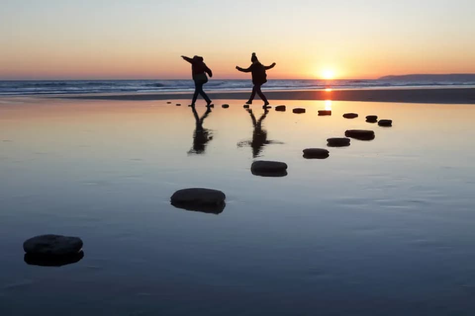 Zwei Personen balancieren auf Stämmen im Wasser.