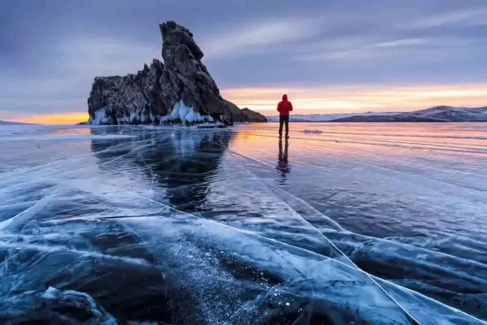 Ein Mann steht auf einem gefrorenen See mit einer beeindruckenden Felsformation im Hintergrund.